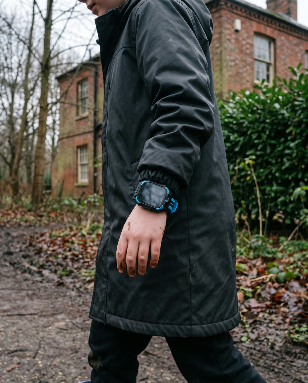 A child crossing a muddy woodland path on a grey afternoon, wearing the watch