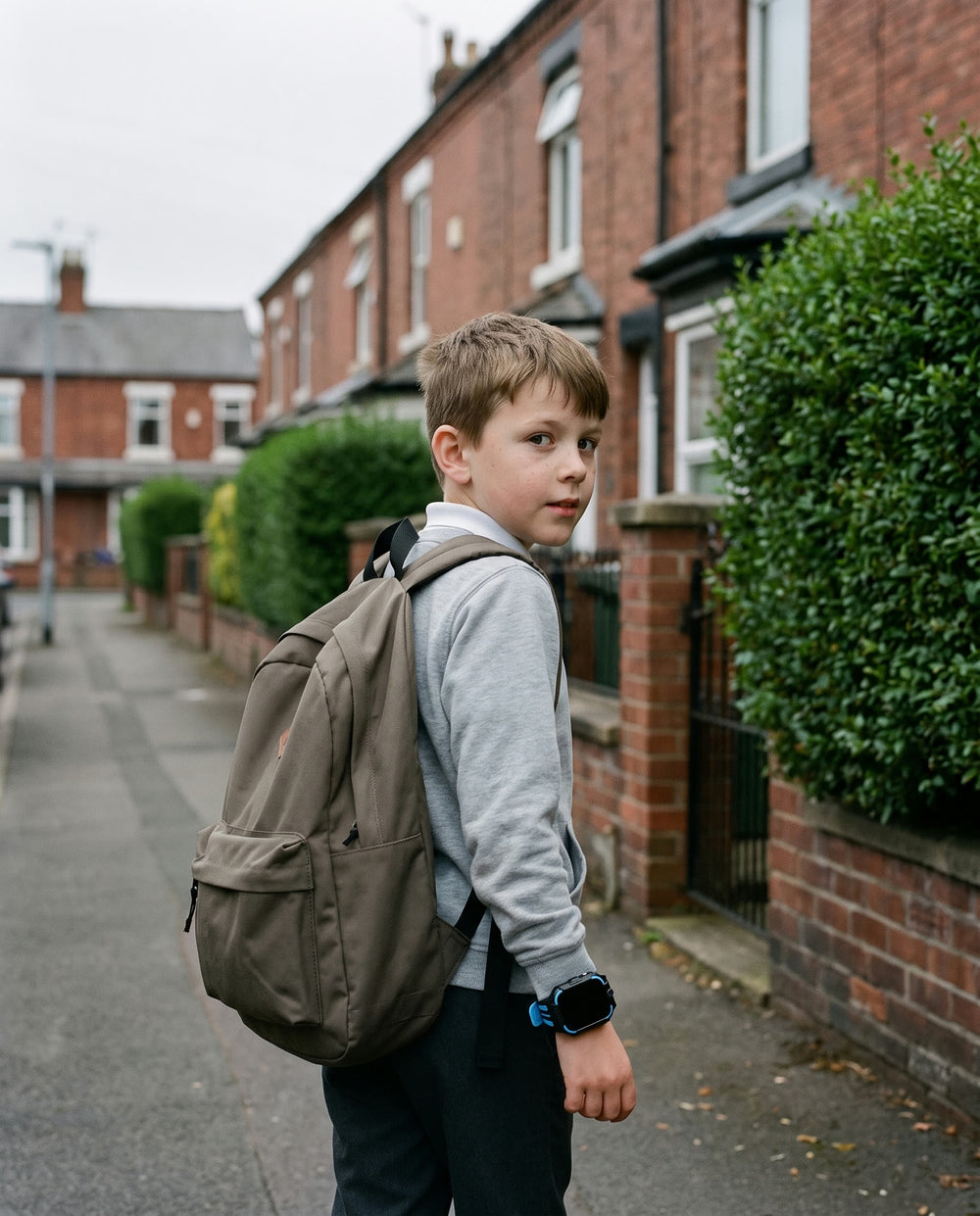 A boy walking away down a quiet British residential street with his backpack